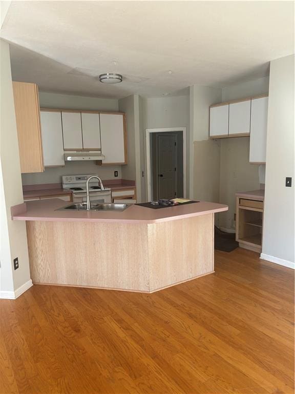 kitchen featuring light wood finished floors, white cabinets, a sink, a peninsula, and baseboards