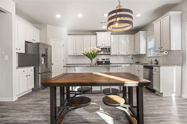 kitchen with light stone countertops, stainless steel appliances, dark wood-type flooring, decorative light fixtures, and white cabinetry