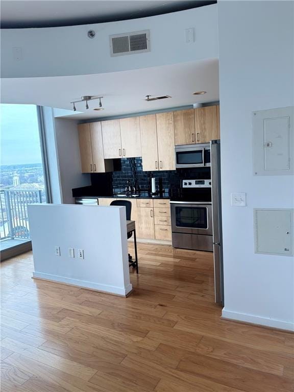 kitchen with light hardwood / wood-style flooring, stainless steel appliances, electric panel, tasteful backsplash, and light brown cabinetry