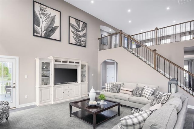 living room with arched walkways, a high ceiling, carpet floors, baseboards, and stairs