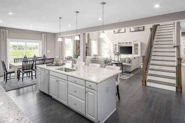 kitchen featuring a sink, dishwasher, light stone counters, recessed lighting, and a kitchen island with sink