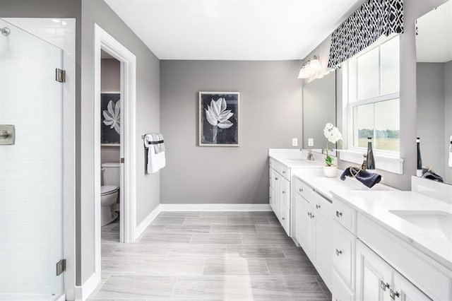bathroom featuring baseboards, double vanity, a sink, a shower stall, and toilet