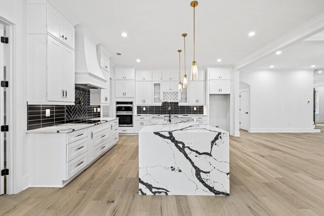 kitchen with white cabinetry, premium range hood, a large island with sink, and light hardwood / wood-style floors