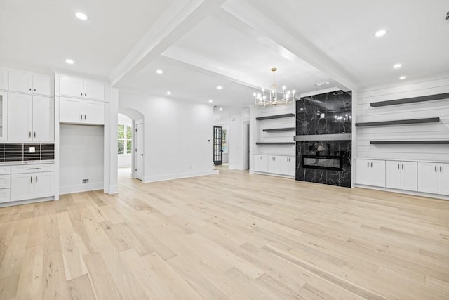 unfurnished living room featuring a premium fireplace, light hardwood / wood-style flooring, a chandelier, and beam ceiling