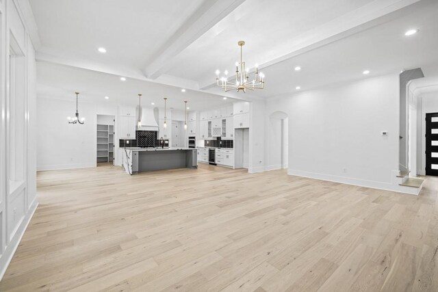 unfurnished living room featuring light hardwood / wood-style floors, beam ceiling, and an inviting chandelier