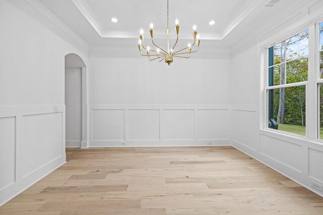 unfurnished dining area with ornamental molding, light hardwood / wood-style flooring, a notable chandelier, and a tray ceiling