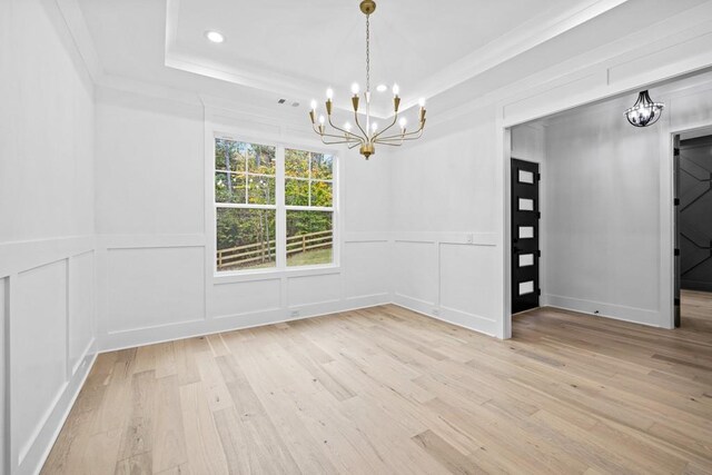 empty room featuring ornamental molding, light hardwood / wood-style floors, a raised ceiling, and an inviting chandelier