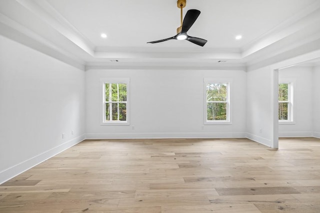 unfurnished room featuring ornamental molding, light wood-type flooring, a healthy amount of sunlight, and a tray ceiling