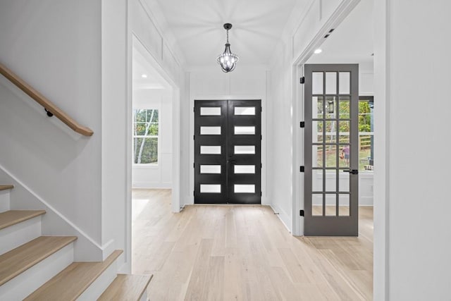 foyer with french doors, a chandelier, and light wood-type flooring