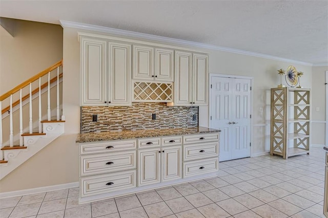 kitchen featuring backsplash, light tile patterned flooring, light stone countertops, cream cabinetry, and ornamental molding