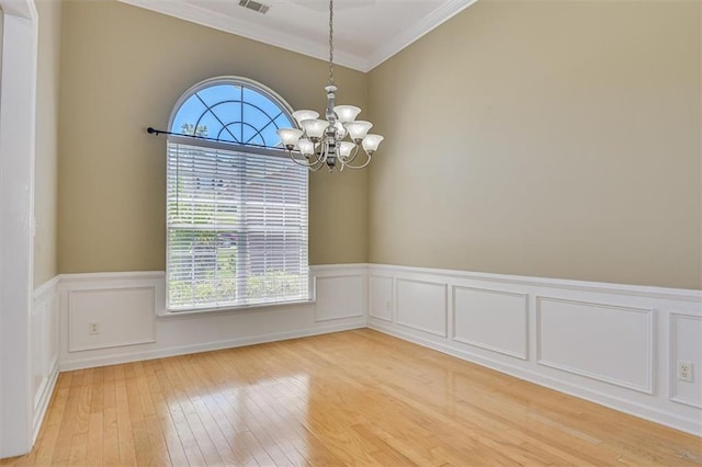 unfurnished room featuring ornamental molding, a chandelier, light wood-style flooring, and a wainscoted wall