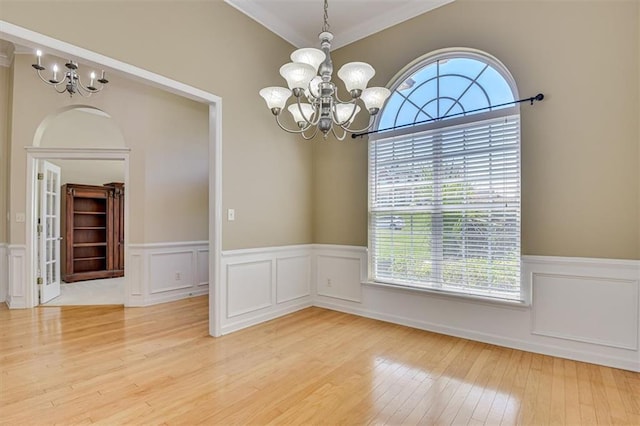unfurnished dining area with a chandelier, hardwood / wood-style flooring, wainscoting, crown molding, and a decorative wall