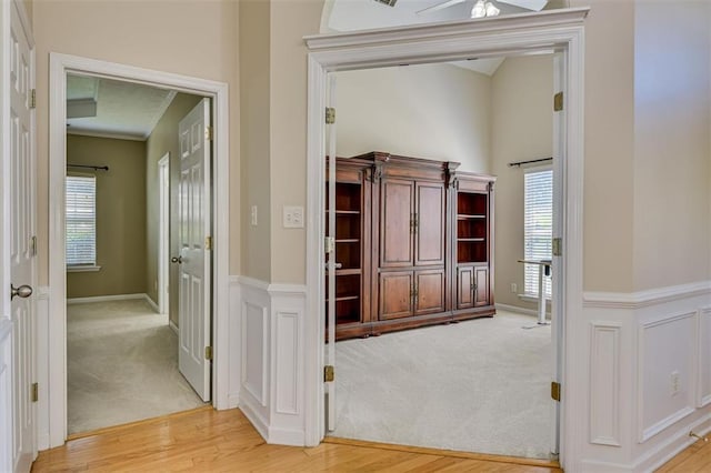 corridor featuring light colored carpet, light wood finished floors, crown molding, and baseboards