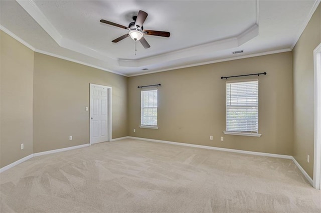 spare room with a tray ceiling, crown molding, ceiling fan, light colored carpet, and baseboards