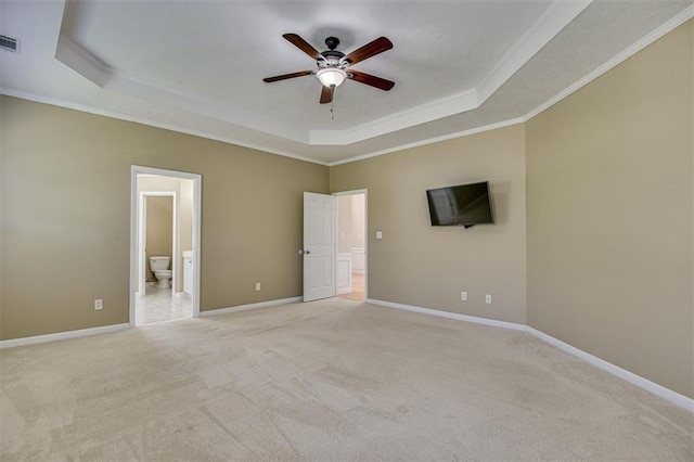 unfurnished bedroom featuring a raised ceiling, crown molding, light colored carpet, ensuite bath, and baseboards