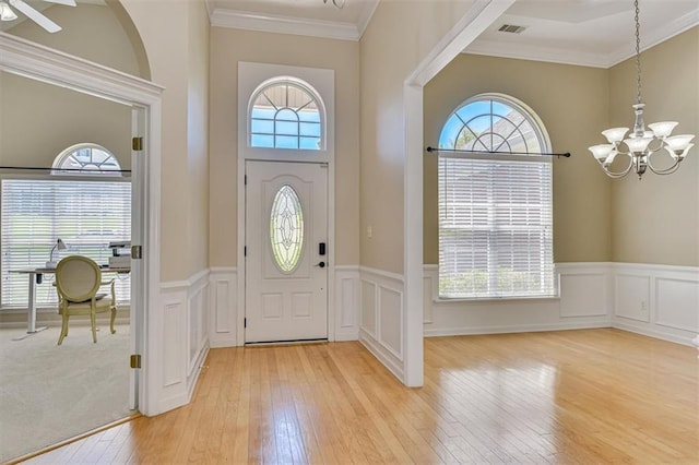 entrance foyer with a chandelier, light wood-style floors, crown molding, a wainscoted wall, and a decorative wall