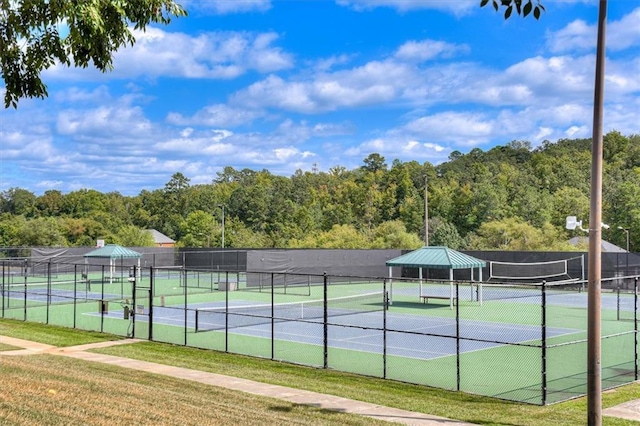 view of tennis court featuring fence and a wooded view