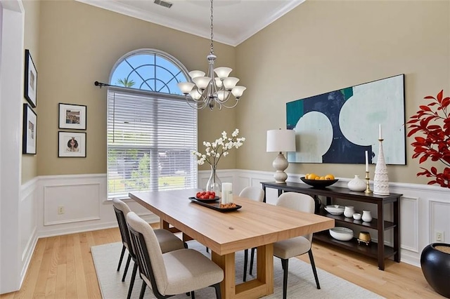dining room with a chandelier, ornamental molding, healthy amount of natural light, light wood finished floors, and a wainscoted wall