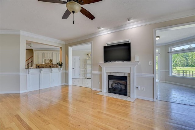 unfurnished living room featuring a ceiling fan, wood finished floors, a tile fireplace, ornamental molding, and stairs