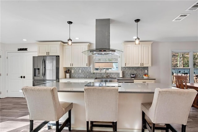 kitchen featuring a kitchen island, decorative light fixtures, exhaust hood, stainless steel fridge with ice dispenser, and cream cabinetry