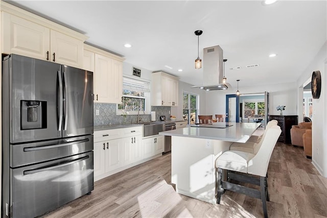 kitchen with sink, appliances with stainless steel finishes, cream cabinets, island range hood, and decorative light fixtures