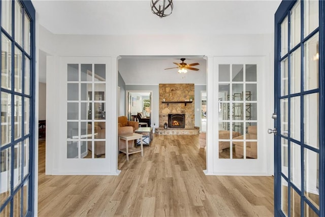 interior space featuring ceiling fan, a fireplace, light hardwood / wood-style floors, and french doors