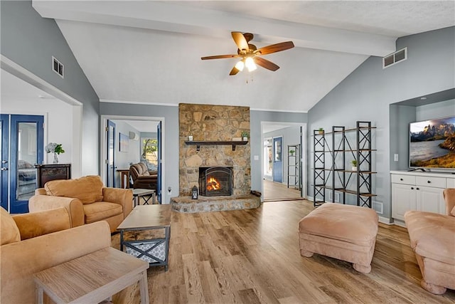 living room with ceiling fan, a stone fireplace, vaulted ceiling with beams, and light wood-type flooring