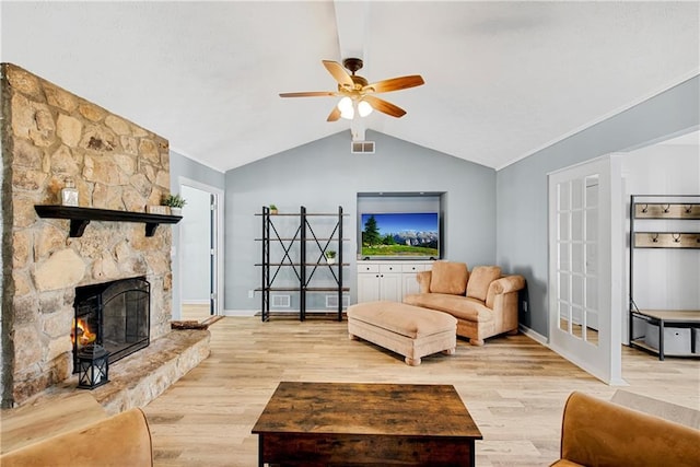 living room with vaulted ceiling, a stone fireplace, ceiling fan, and light hardwood / wood-style floors