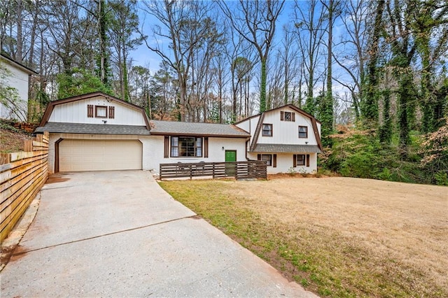 view of front of property with a front yard, concrete driveway, fence, and a gambrel roof