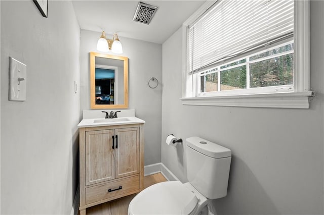 half bathroom with baseboards, visible vents, toilet, wood finished floors, and vanity