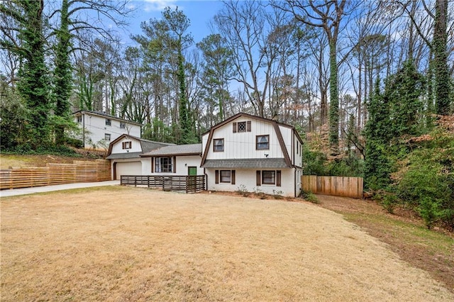 rear view of house featuring brick siding, fence, a gambrel roof, driveway, and a lawn