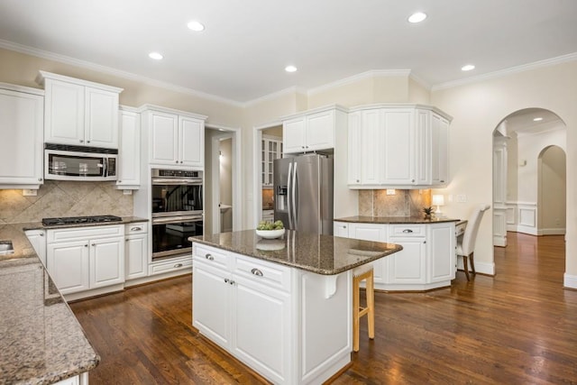 kitchen with appliances with stainless steel finishes, arched walkways, white cabinets, and dark wood-style floors