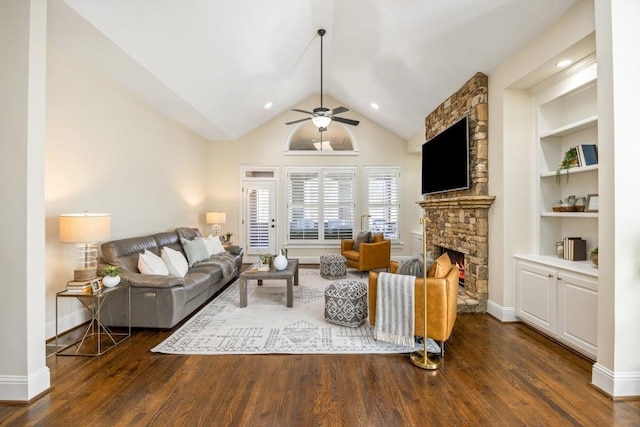 living room with built in shelves, dark wood finished floors, a ceiling fan, vaulted ceiling, and a stone fireplace