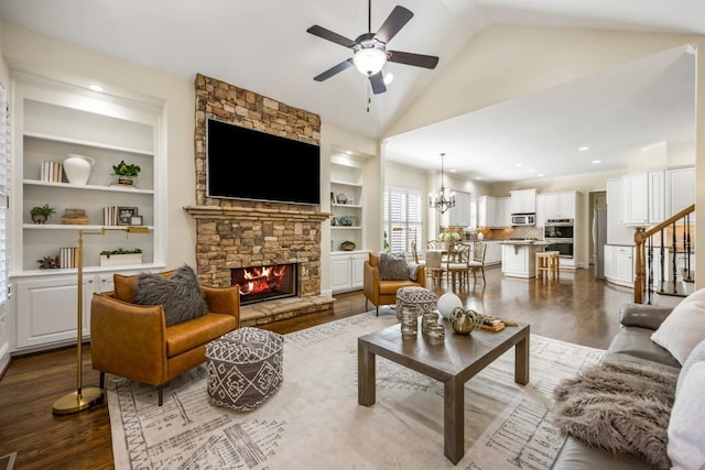 living room featuring lofted ceiling, ceiling fan with notable chandelier, a fireplace, stairs, and dark wood-style floors