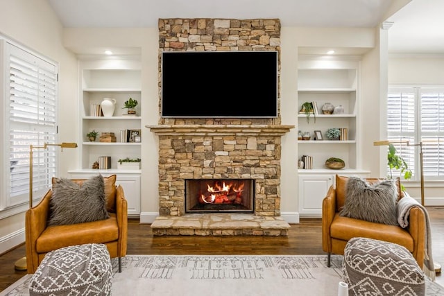 sitting room featuring built in shelves, a fireplace, and wood finished floors