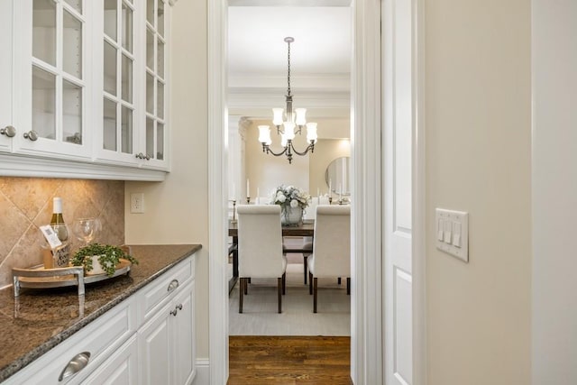 bar featuring a notable chandelier, crown molding, backsplash, dark wood-style floors, and pendant lighting