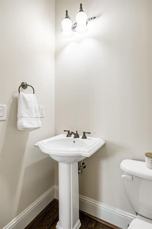 half bathroom featuring wood finished floors, toilet, and baseboards