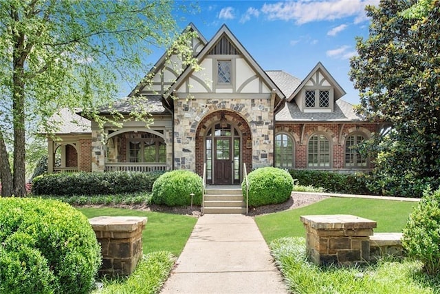 english style home featuring brick siding, roof with shingles, a front lawn, and stucco siding