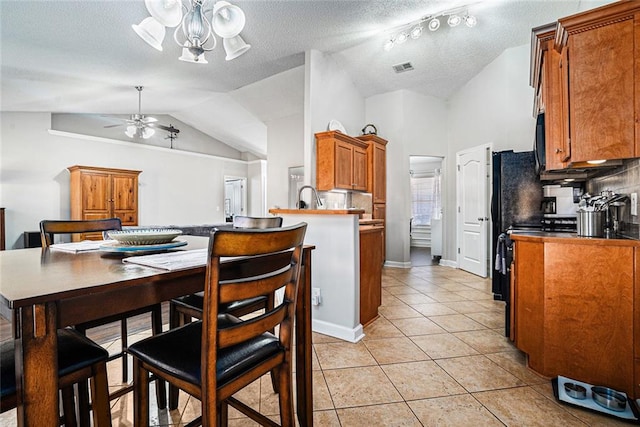 kitchen with brown cabinets, tasteful backsplash, lofted ceiling, light tile patterned flooring, and ceiling fan with notable chandelier