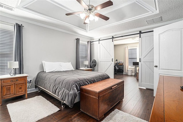 bedroom featuring dark wood-style floors, a tray ceiling, a barn door, and visible vents