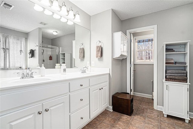 full bathroom featuring double vanity, a stall shower, visible vents, a textured ceiling, and a sink