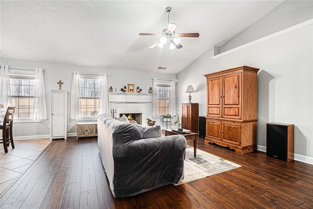 living area featuring dark wood-type flooring, visible vents, baseboards, vaulted ceiling, and a brick fireplace