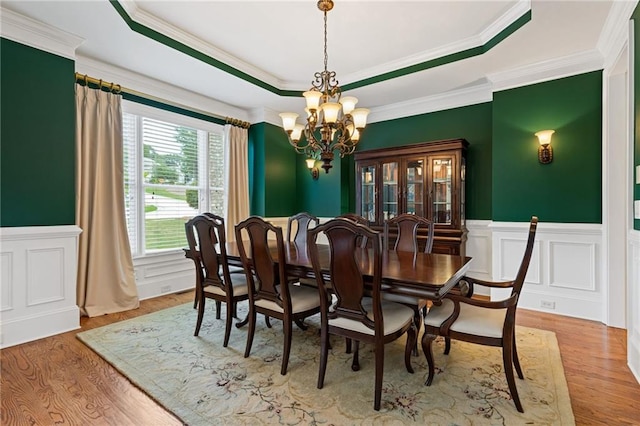 dining room with a tray ceiling, ornamental molding, light hardwood / wood-style flooring, and a notable chandelier