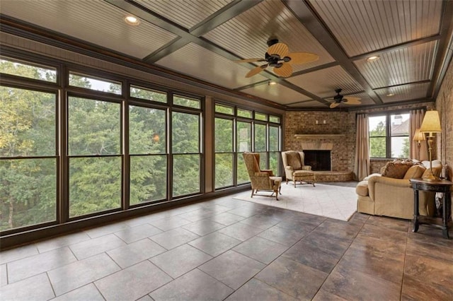 unfurnished sunroom featuring wooden ceiling, coffered ceiling, ceiling fan, and a brick fireplace