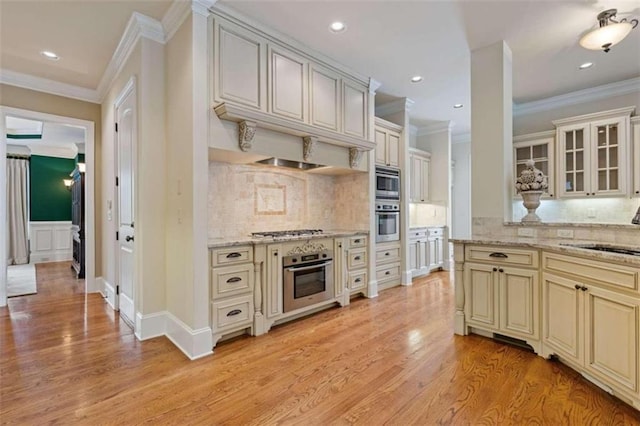 kitchen with appliances with stainless steel finishes, light wood-type flooring, cream cabinets, and light stone counters