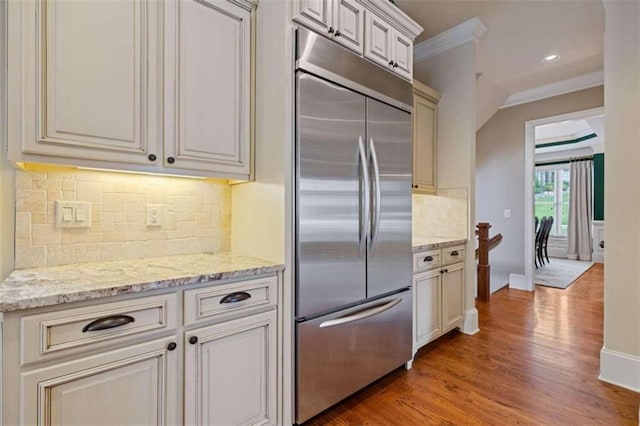 kitchen with light hardwood / wood-style floors, built in refrigerator, tasteful backsplash, light stone countertops, and crown molding