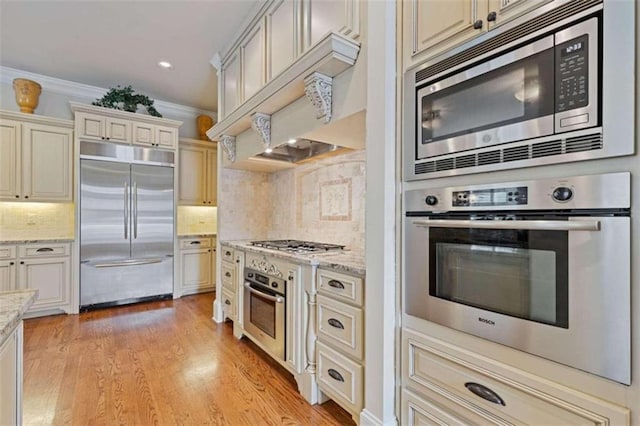 kitchen featuring custom range hood, light hardwood / wood-style floors, tasteful backsplash, built in appliances, and crown molding