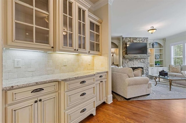 kitchen featuring light wood-type flooring, light stone counters, cream cabinets, and a stone fireplace