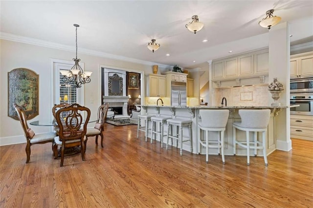 kitchen featuring light wood-type flooring, ornamental molding, appliances with stainless steel finishes, light stone countertops, and cream cabinets