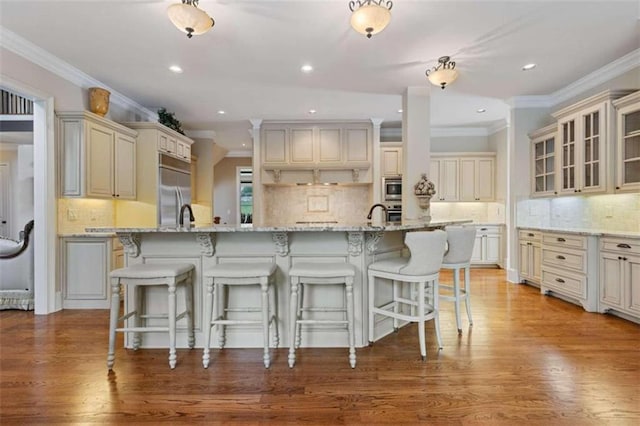 kitchen featuring built in appliances, light stone countertops, a kitchen island with sink, and light hardwood / wood-style floors